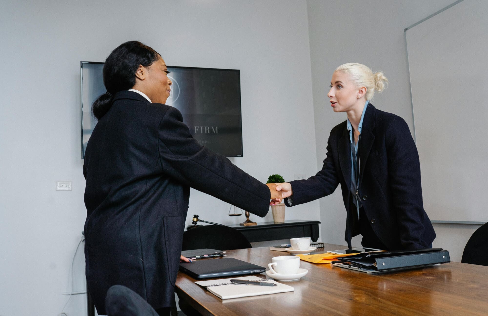 Agreement Two office workers shaking hands over a wooden desk.