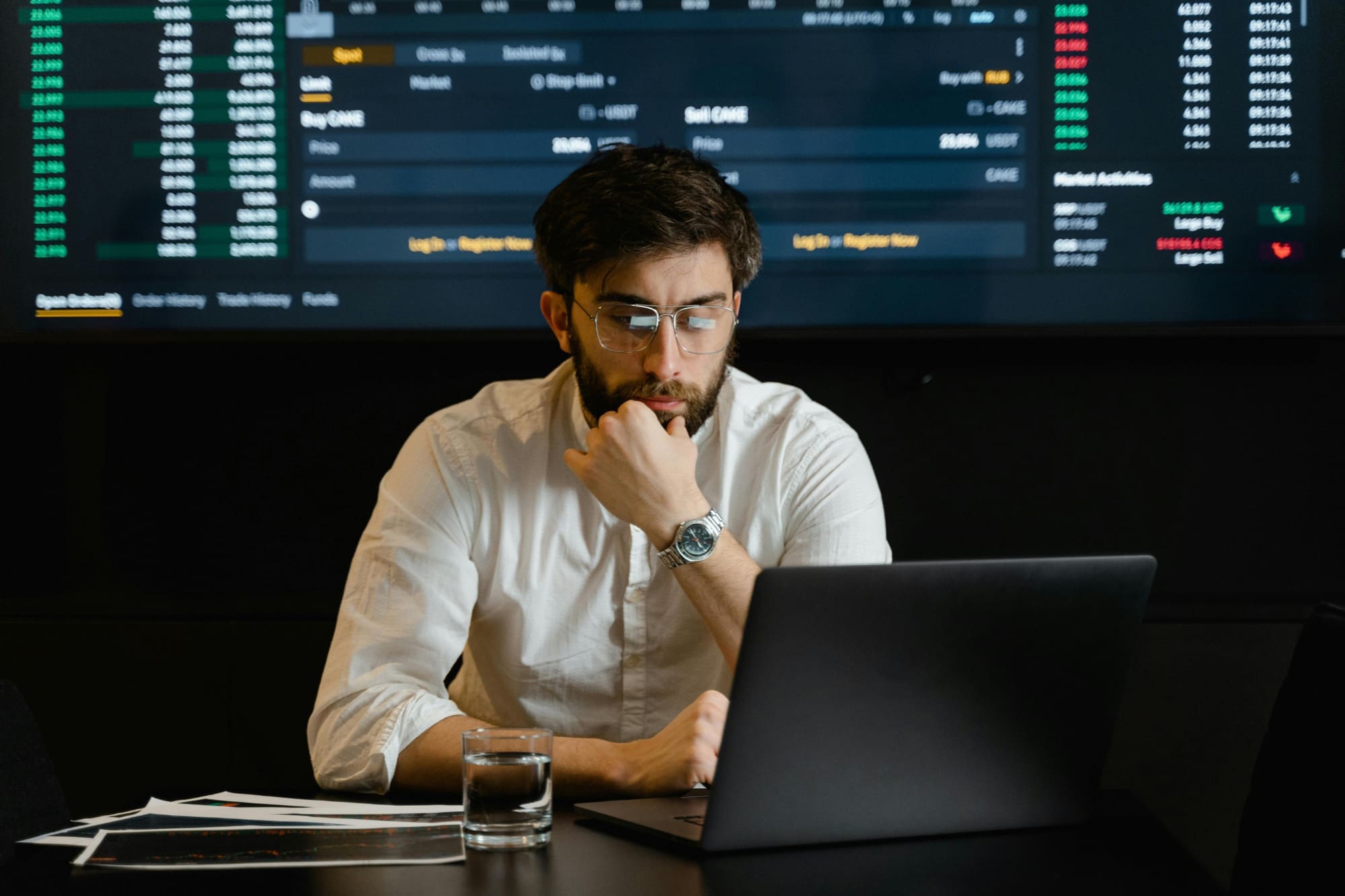Confused-office-worker Office worker sitting at laptop looking confused with graphs on a screen behind him.