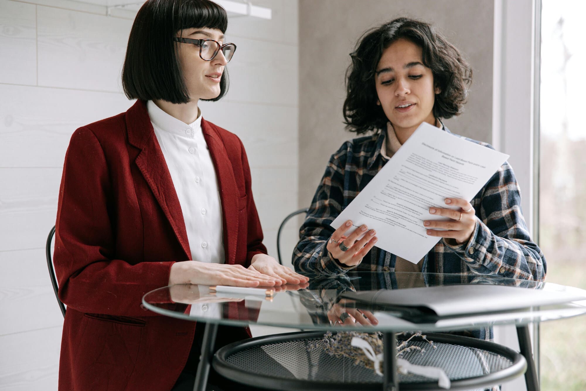 Contract Two people behind round glass table looking at a paper document.