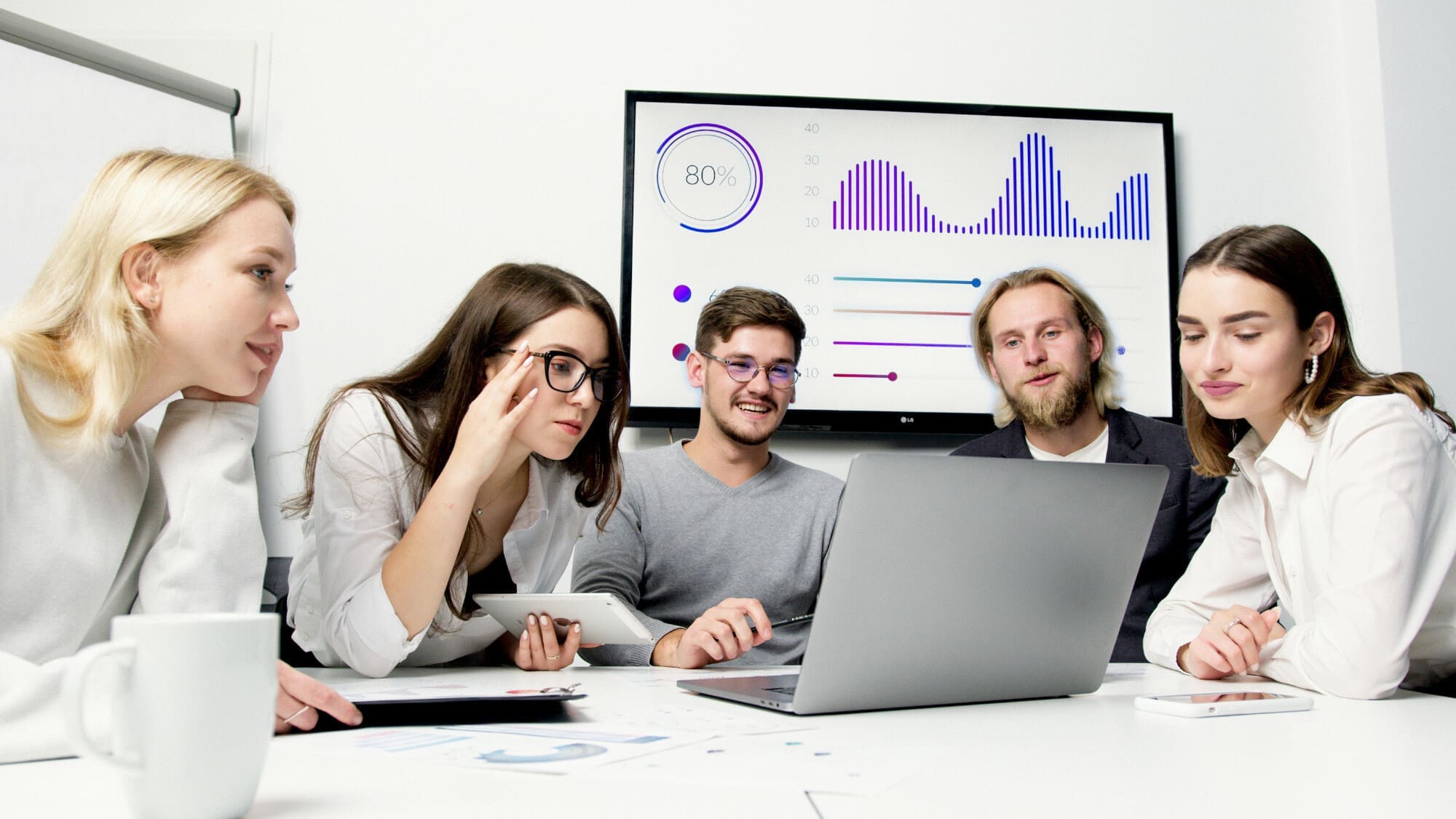 Happy-office Five happy office workers looking at a laptop with a screen showing statistics graphs behind them.