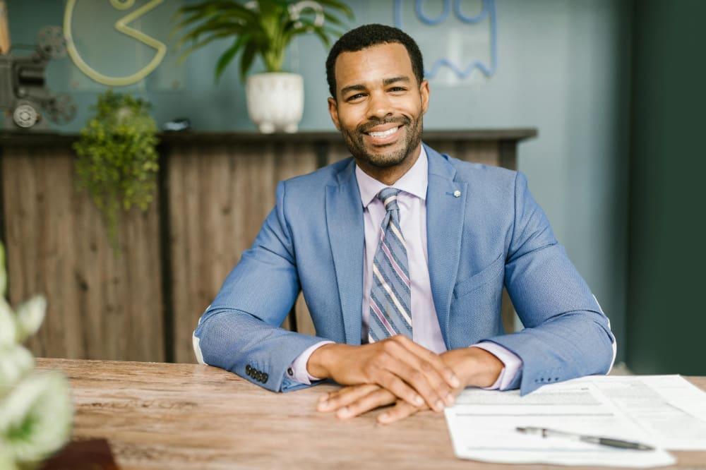 Office-candidate Interview candidate in blue suit smiling with hands resting on wooden desk.