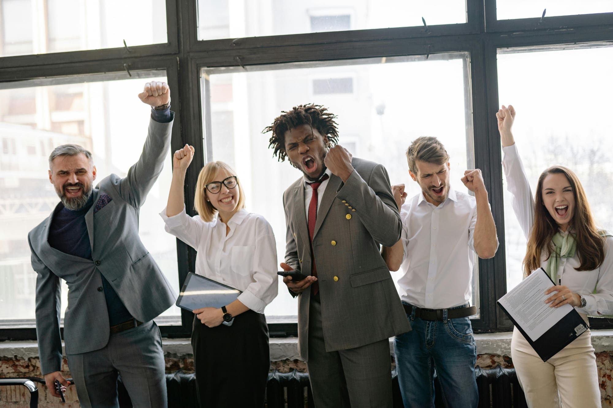 We found them! Five office workers holding clipboards and celebrating with hands in the air.