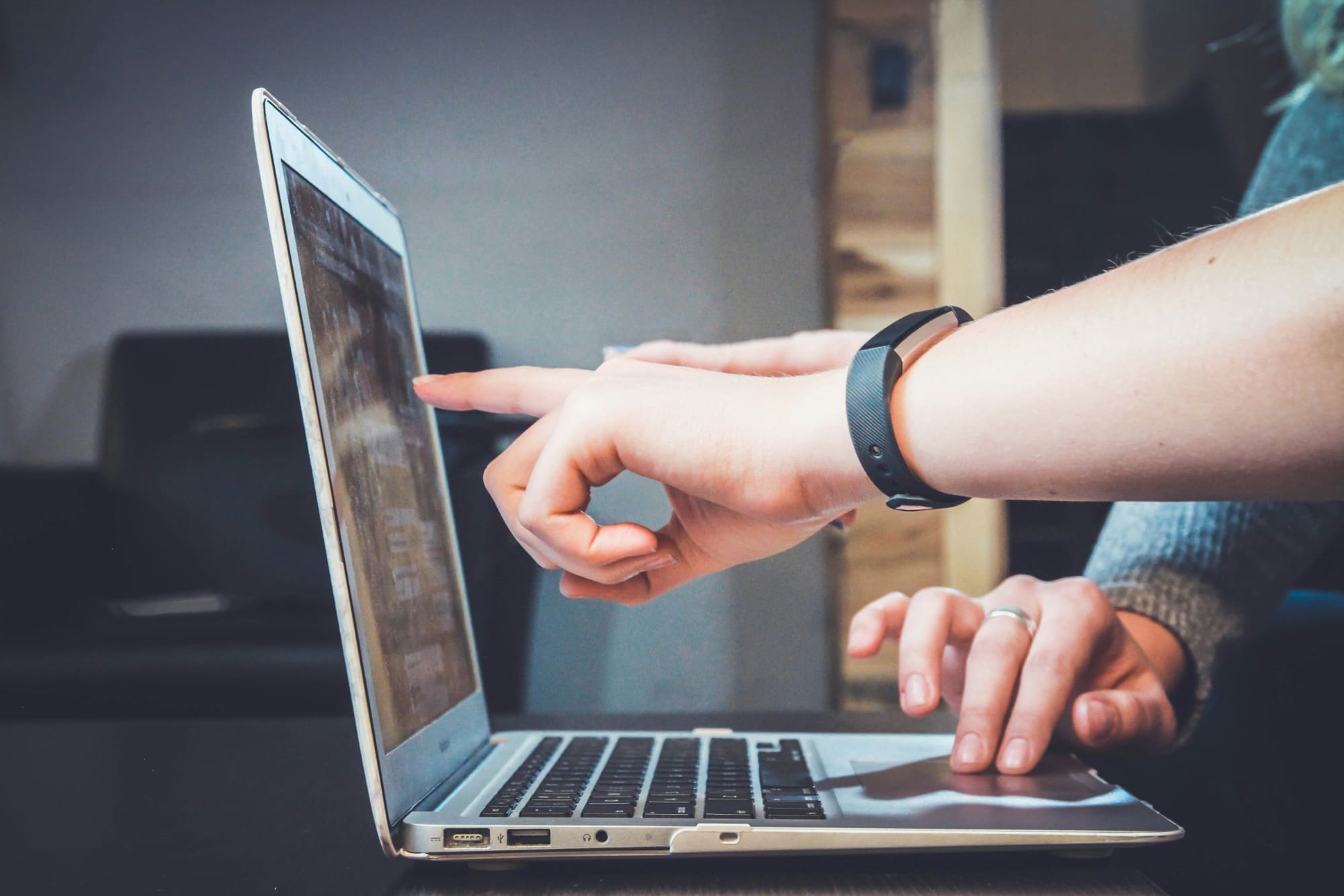Somebody pointing to laptop screen while another person types.