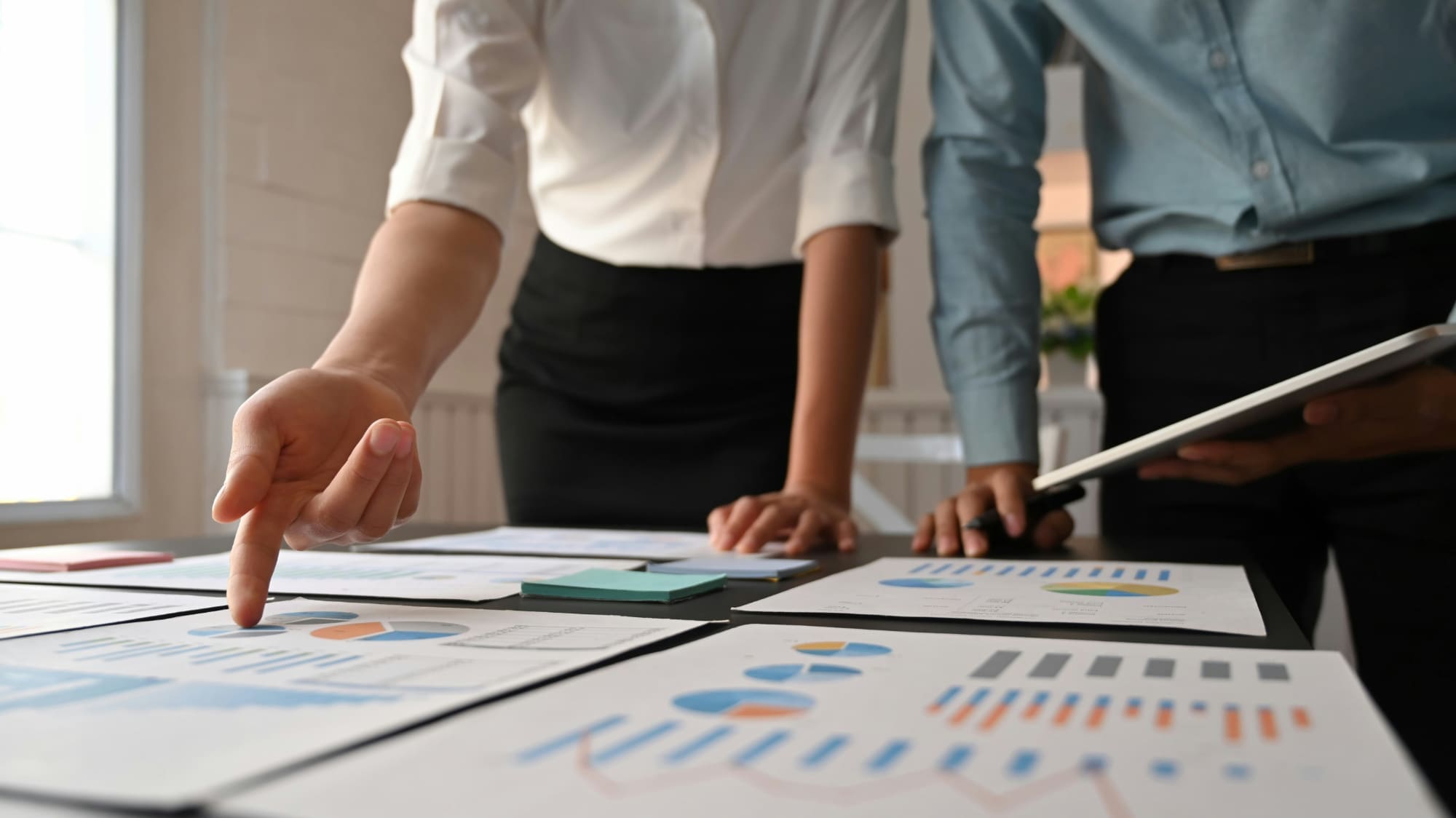 Two business people pointing to desk covered in various business charts.