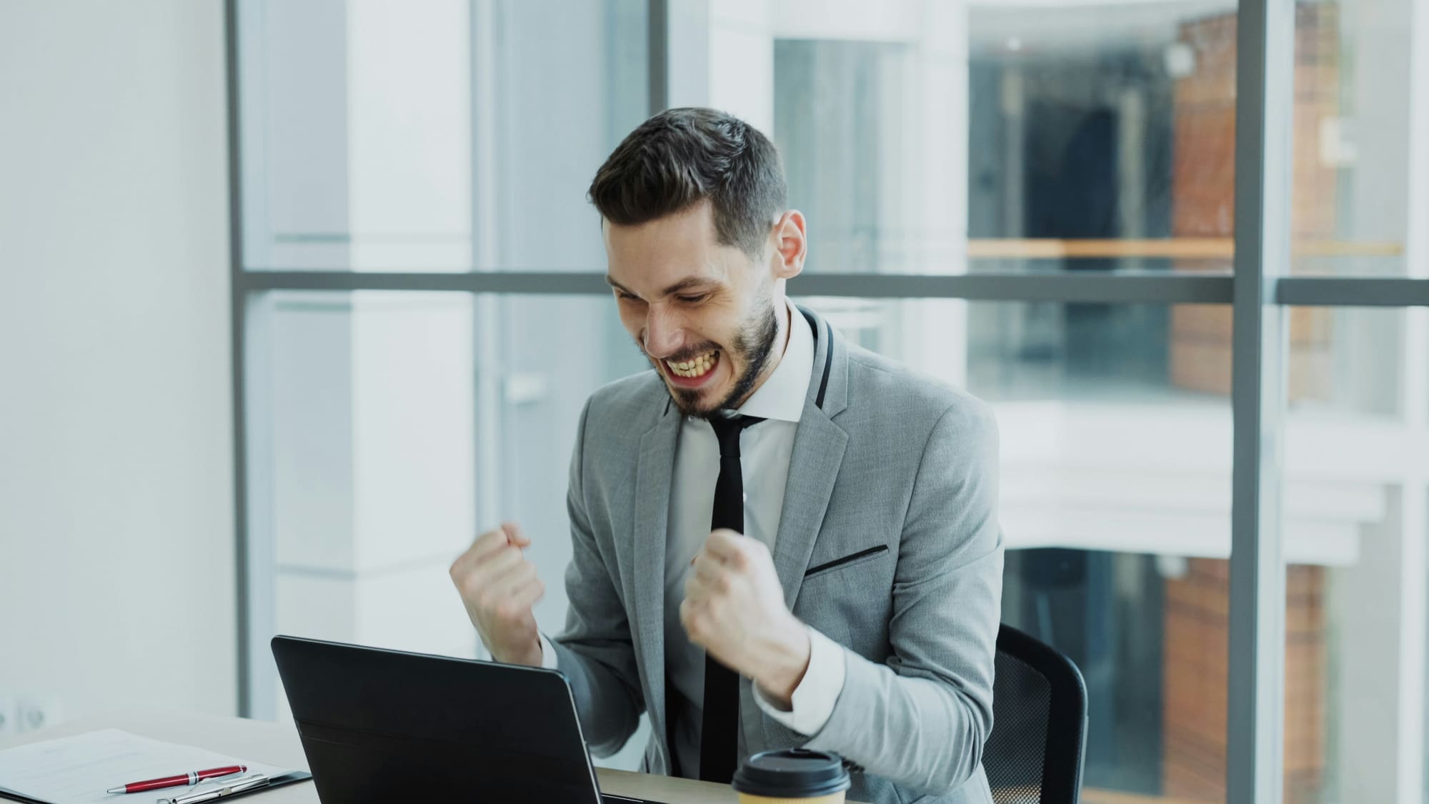 Business person celebrating with clenched fists behind laptop while sitting at desk.